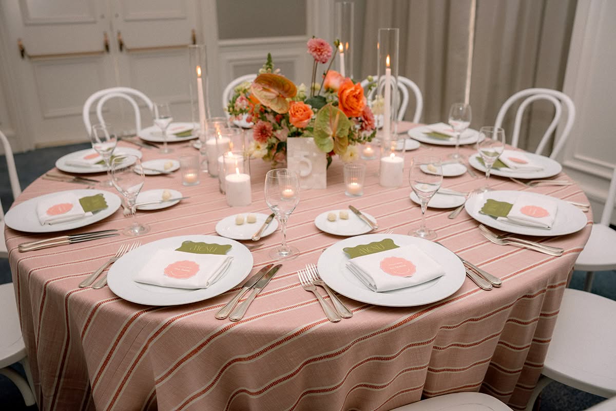 Reception table with blush and rust striped linen, white chairs, taper candles, and a peach and orange floral centerpiece.
