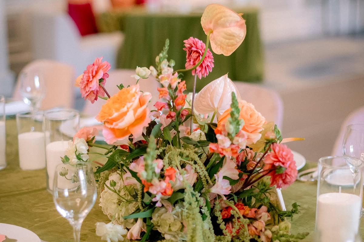 Low centerpiece of peach roses, dahlias, and anthurium on an olive green linen with place settings.