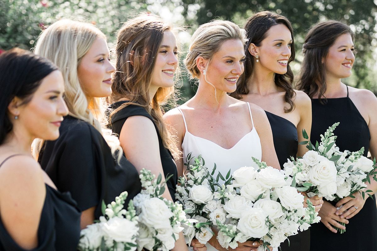 Claire with her bridesmaids in black gowns, each holding a white floral bouquet.