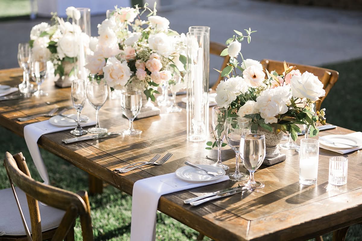 Outdoor reception table with white florals, candles, wood chairs, and natural vineyard-inspired styling.