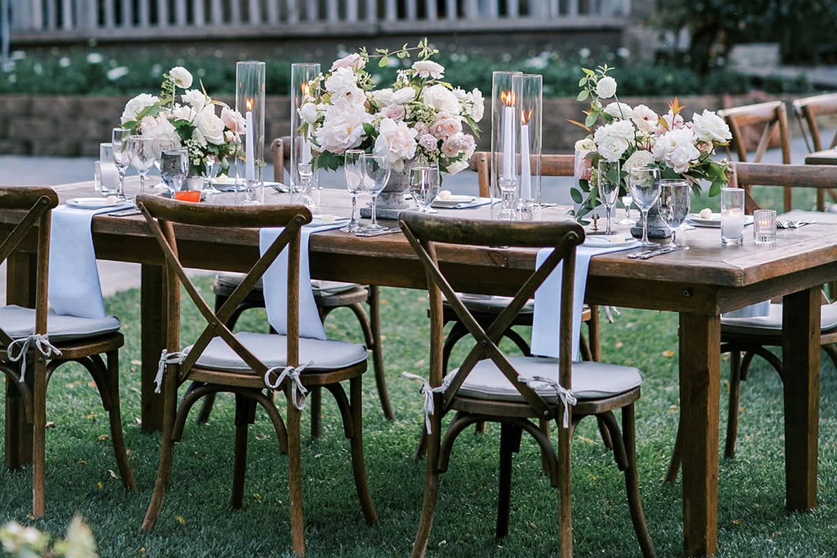 Rustic reception table set beside stone architecture with soft white floral details.
