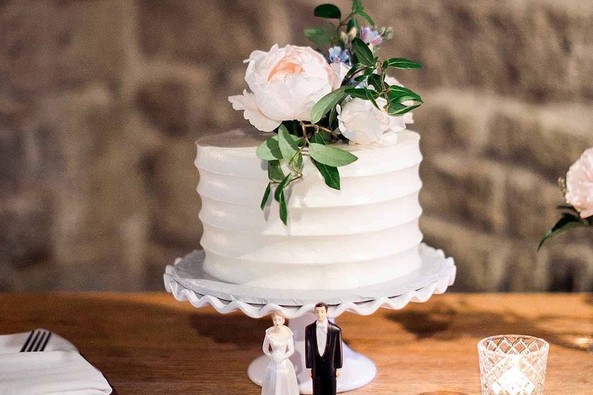 White wedding cake displayed on a rustic wooden table with soft floral accents.