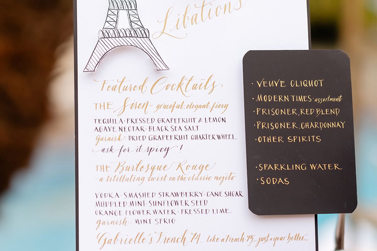 A Parisian-inspired cocktail menu sign with an Eiffel Tower illustration listing the evening's featured drinks.