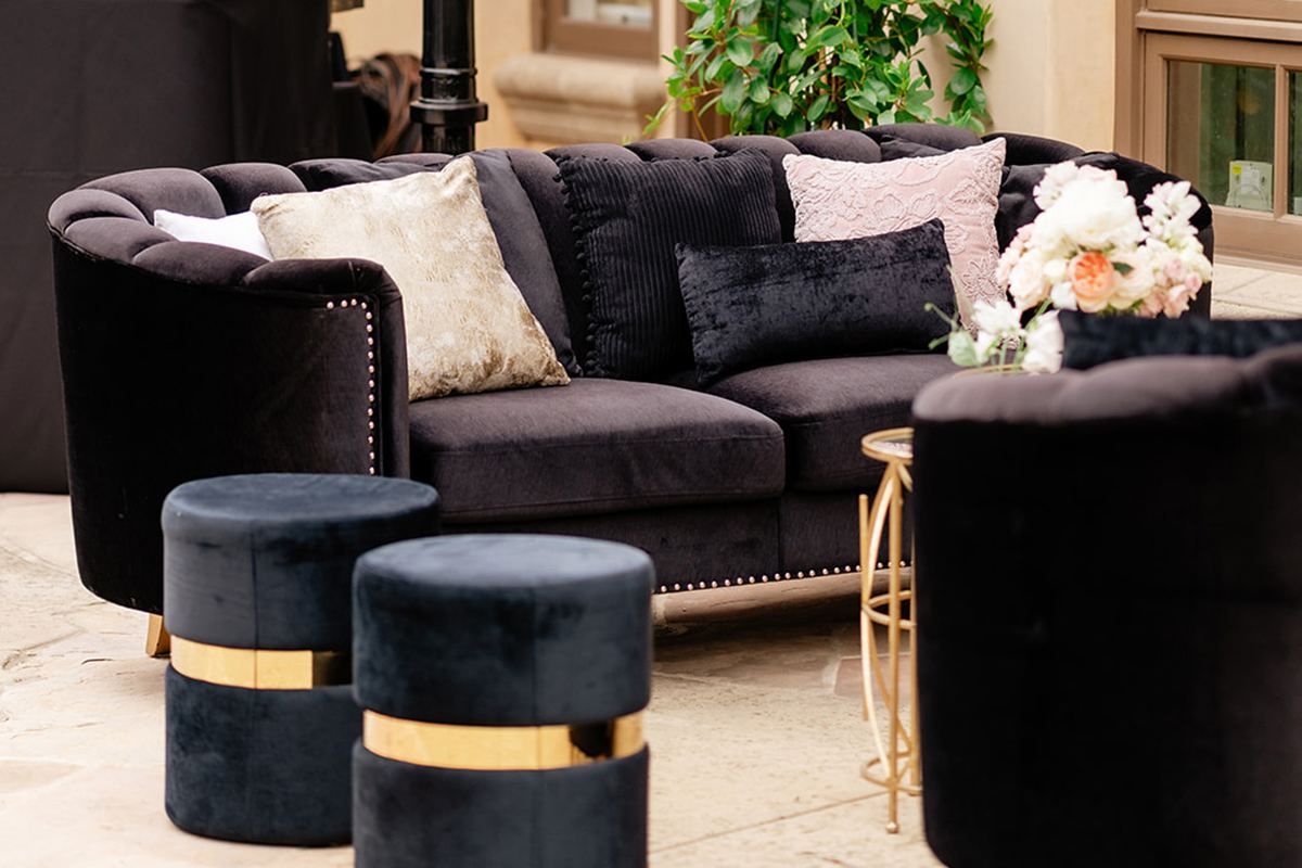 Black velvet lounge seating with gold accents, pillows, florals, and candle lanterns outside a private residence.