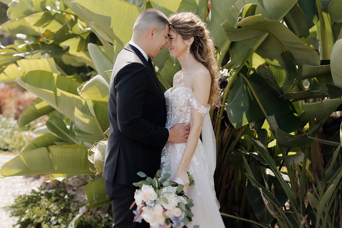 Irma and CJ share a kiss beside tropical greenery during their Coronado wedding portraits.