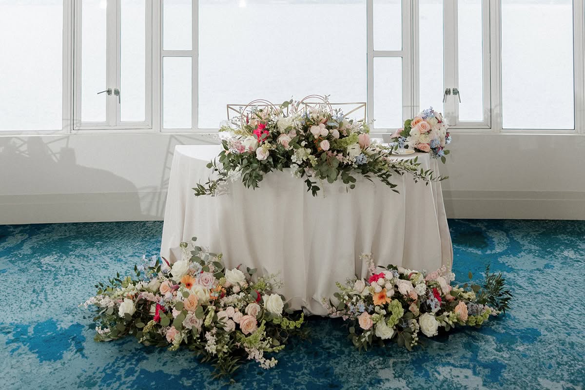 Sweetheart table with soft pink and white florals beneath gold starburst chandeliers at Loews Coronado Bay Resort.