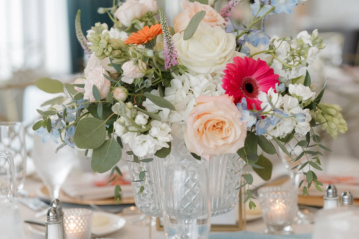 Wedding reception centerpiece with white, blush, and bright pink flowers in a glass vase.