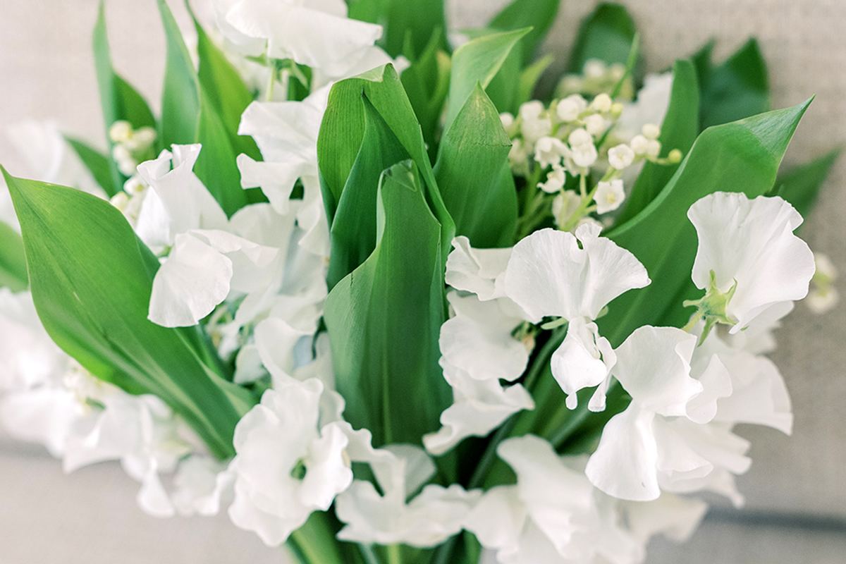 Bridal bouquet of white florals and greenery arranged on a light fabric background.