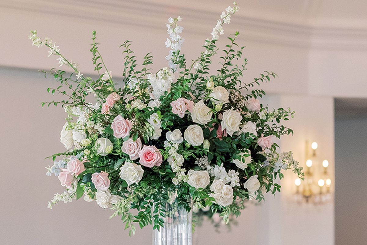 Reception table with a tall pastel floral centerpiece and neutral cane-back chairs.