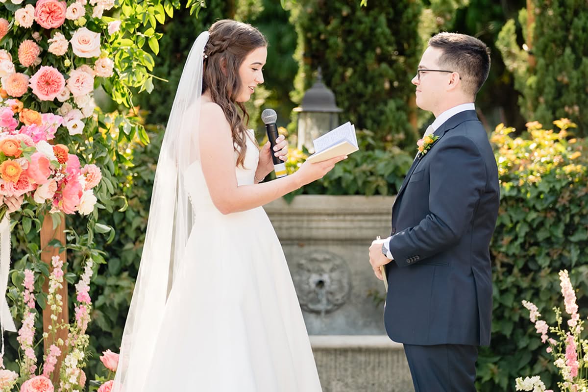 Katie and Jake stand together beneath a colorful floral wedding arch during their Estancia La Jolla ceremony.