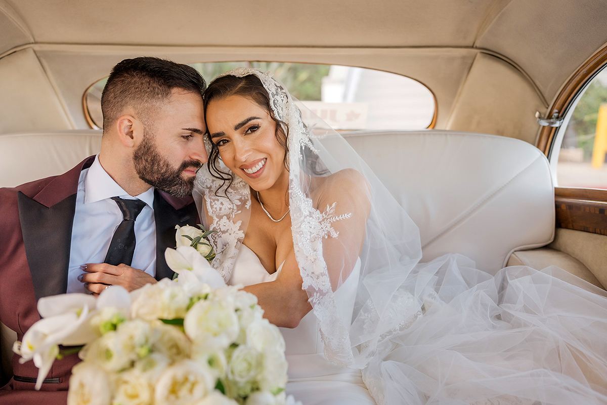 Bride and groom seated together inside a vintage car before their wedding celebration.