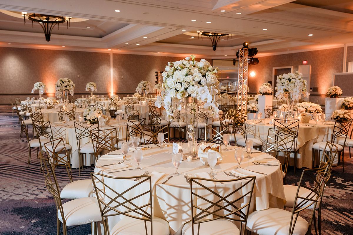 Ballroom reception with gold chairs, white floral centerpieces, and warm lighting.