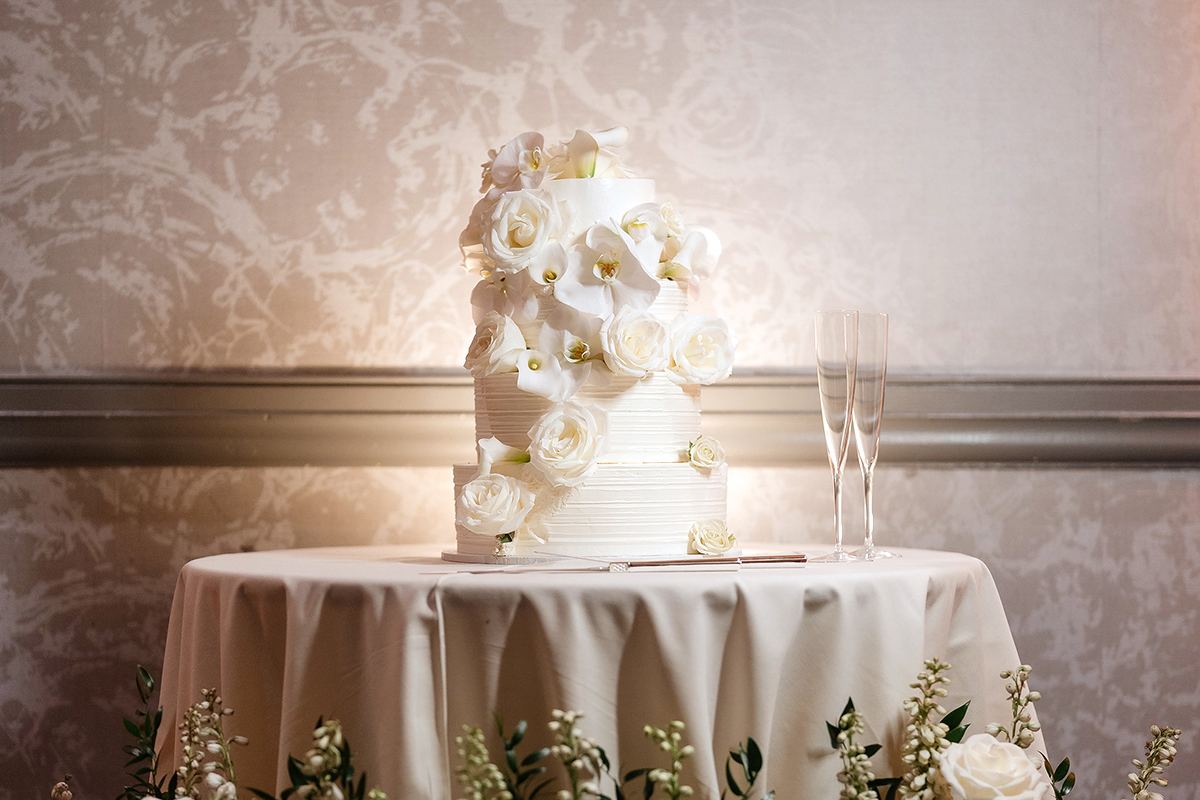 White wedding cake displayed with lush white florals and candlelight.