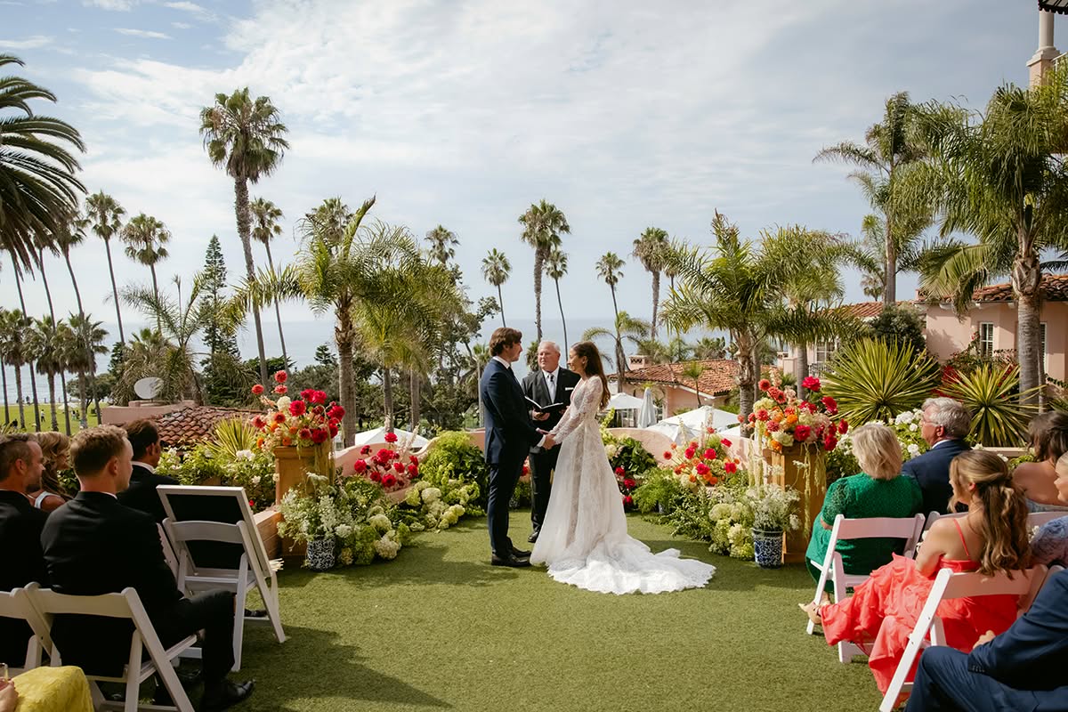 Oi and Halston standing at their ocean-view ceremony surrounded by colorful florals and palm trees.