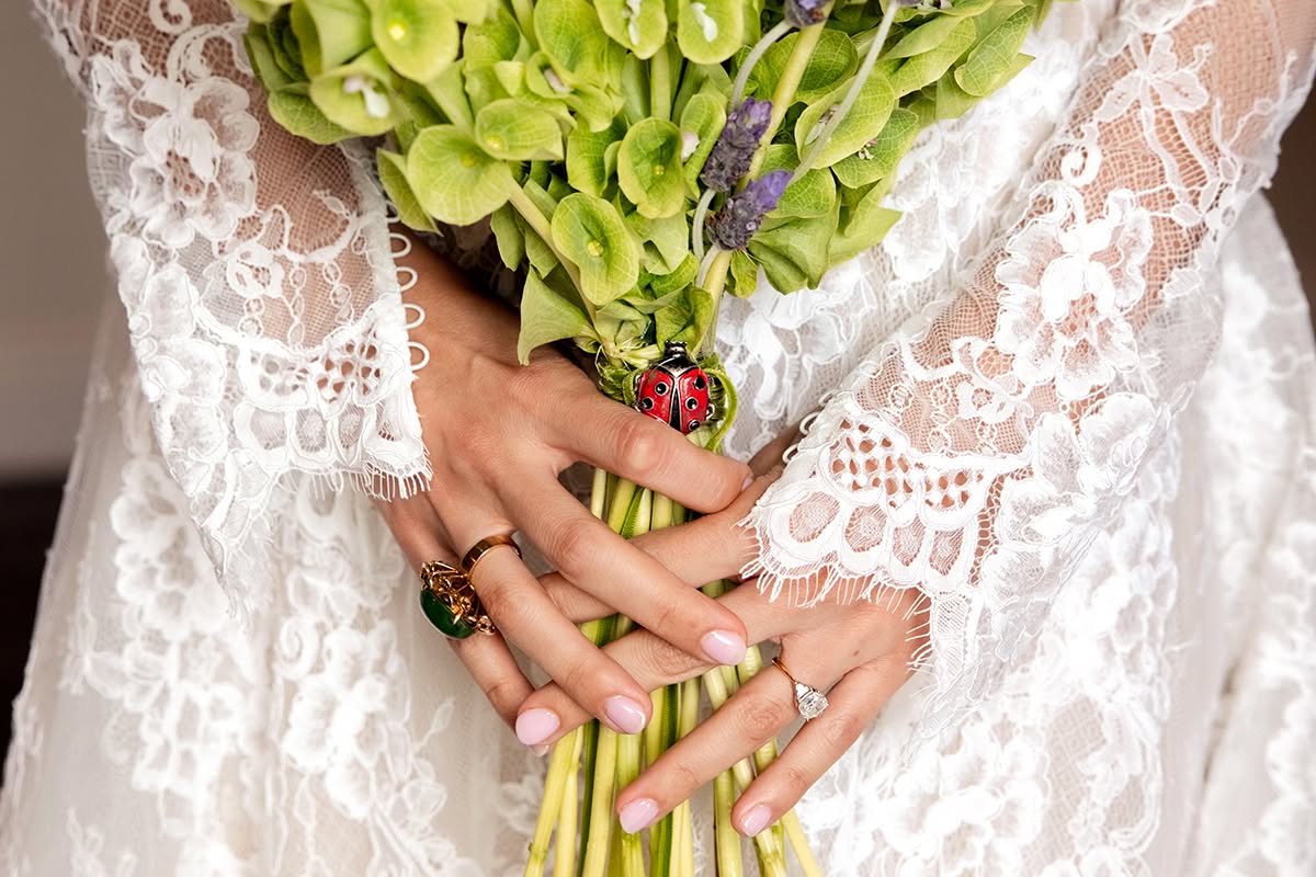 Bride holding a green bouquet against her lace wedding dress.