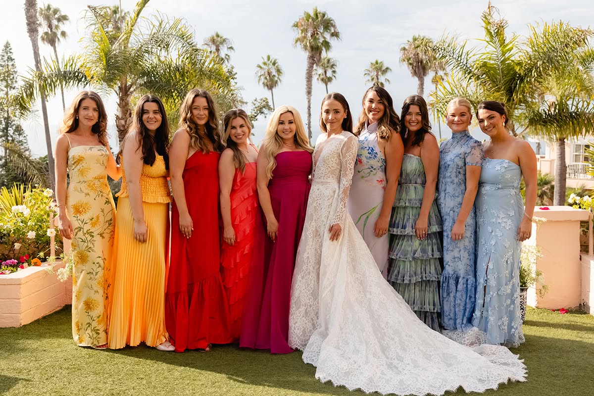 Bride standing with her wedding party in colorful dresses outdoors.