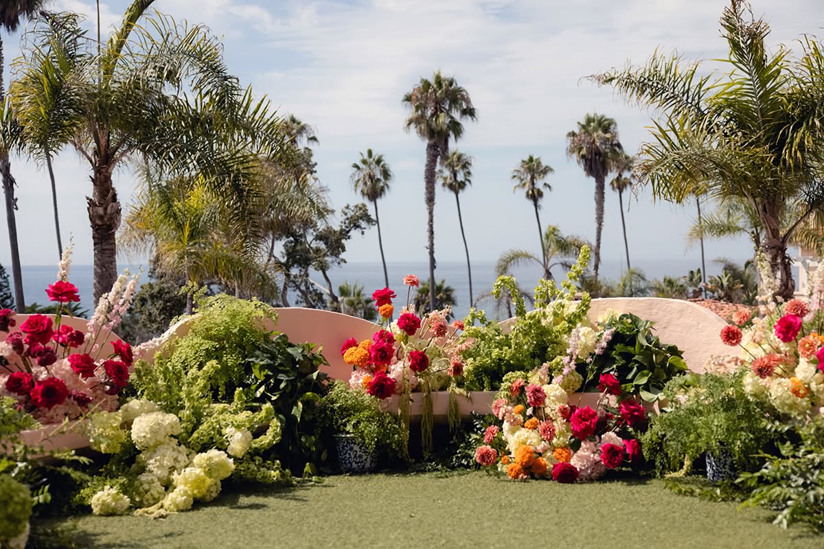 Colorful ceremony flowers and greenery arranged with an ocean and palm tree backdrop.
