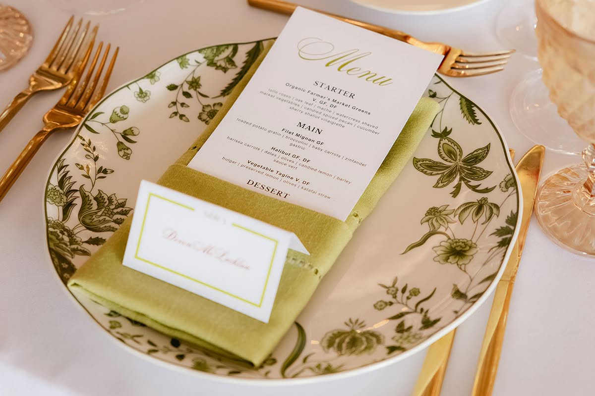 Wedding place setting with menu card, glassware, gold flatware, and floral plate detail.