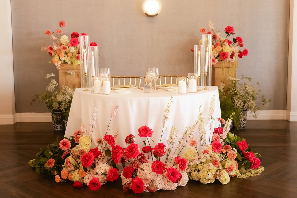 Sweetheart table surrounded by bright floral arrangements and candlelight.