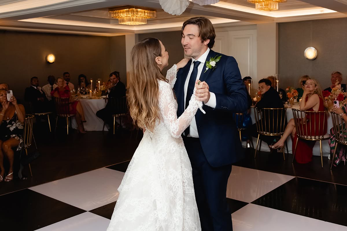 Bride and groom dancing on a black-and-white dance floor beneath colorful hanging décor.