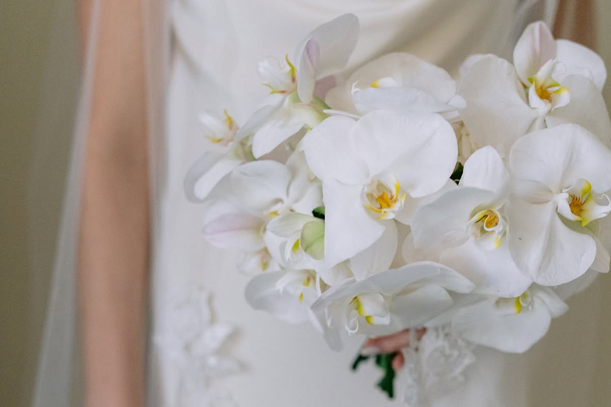 Bride holding a white orchid bouquet against the side of her wedding dress.