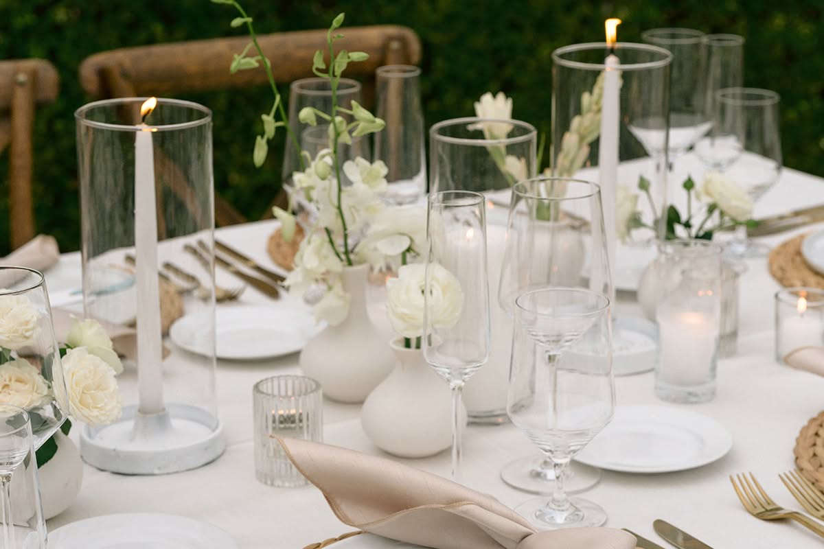 White wedding cake displayed outdoors with white orchid accents and candlelight.